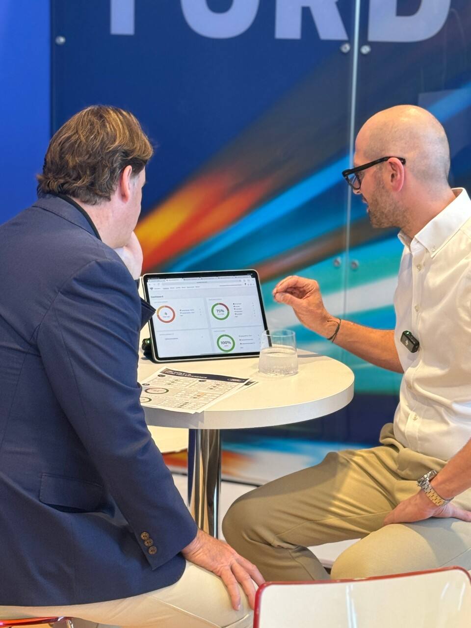 Two men sit at a table and look at a laptop screen